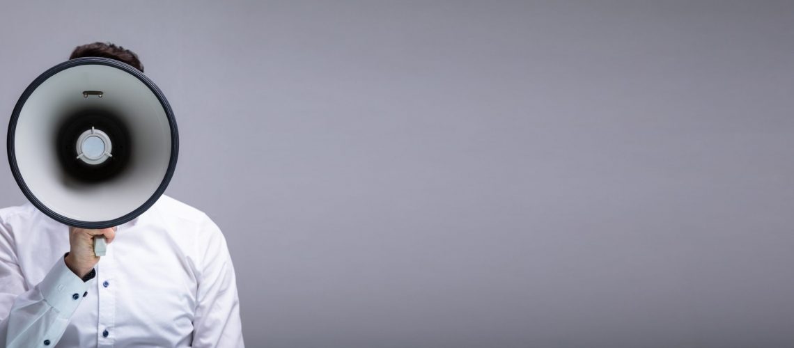 Man Doing Announcement Using Megaphone Against Gray Background